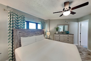 A bedroom with a bed, a ceiling fan, a dresser, a mirror, and a window.