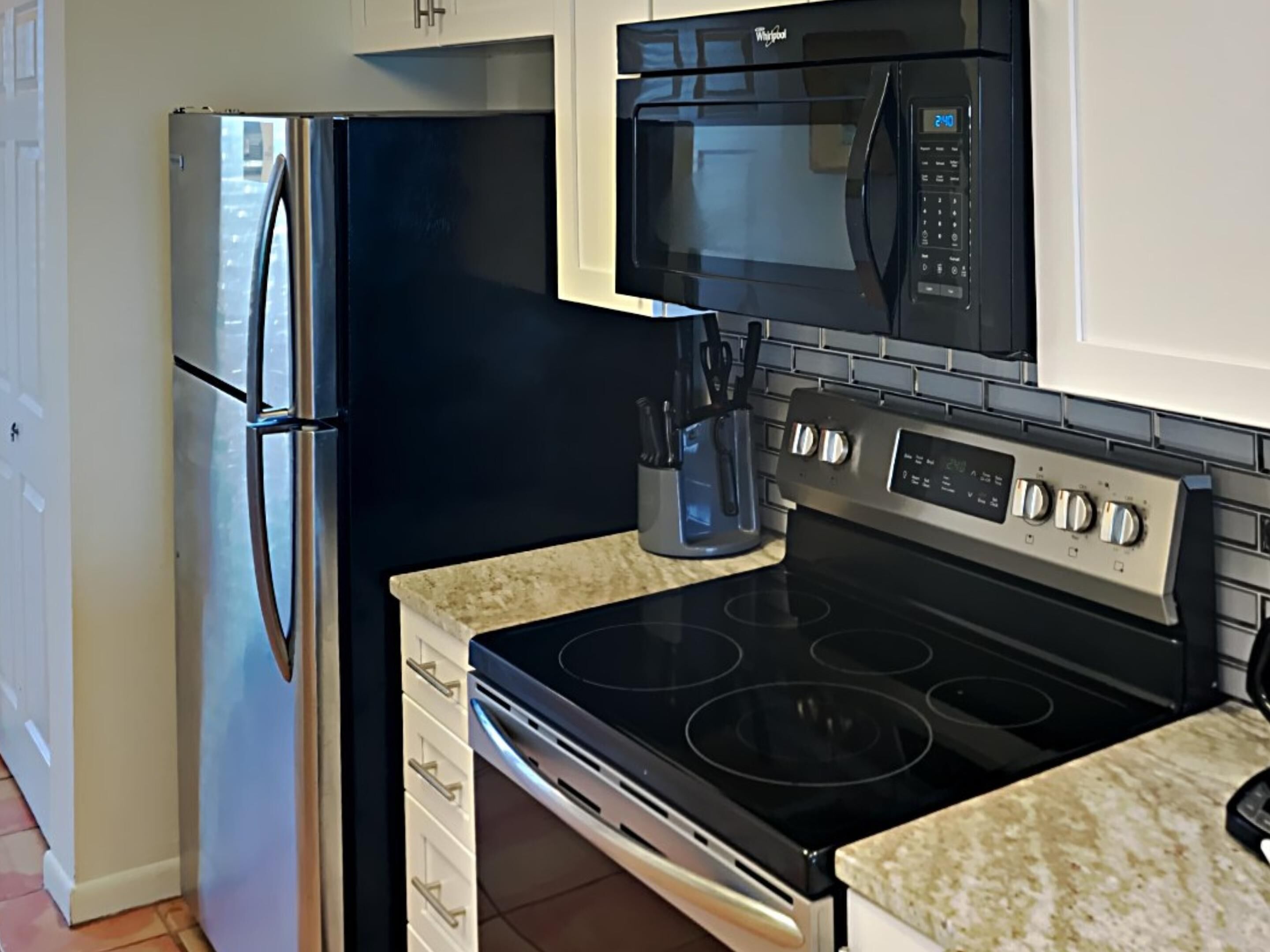 A kitchen with a stainless steel refrigerator, a black microwave, and a black stove with four burners.