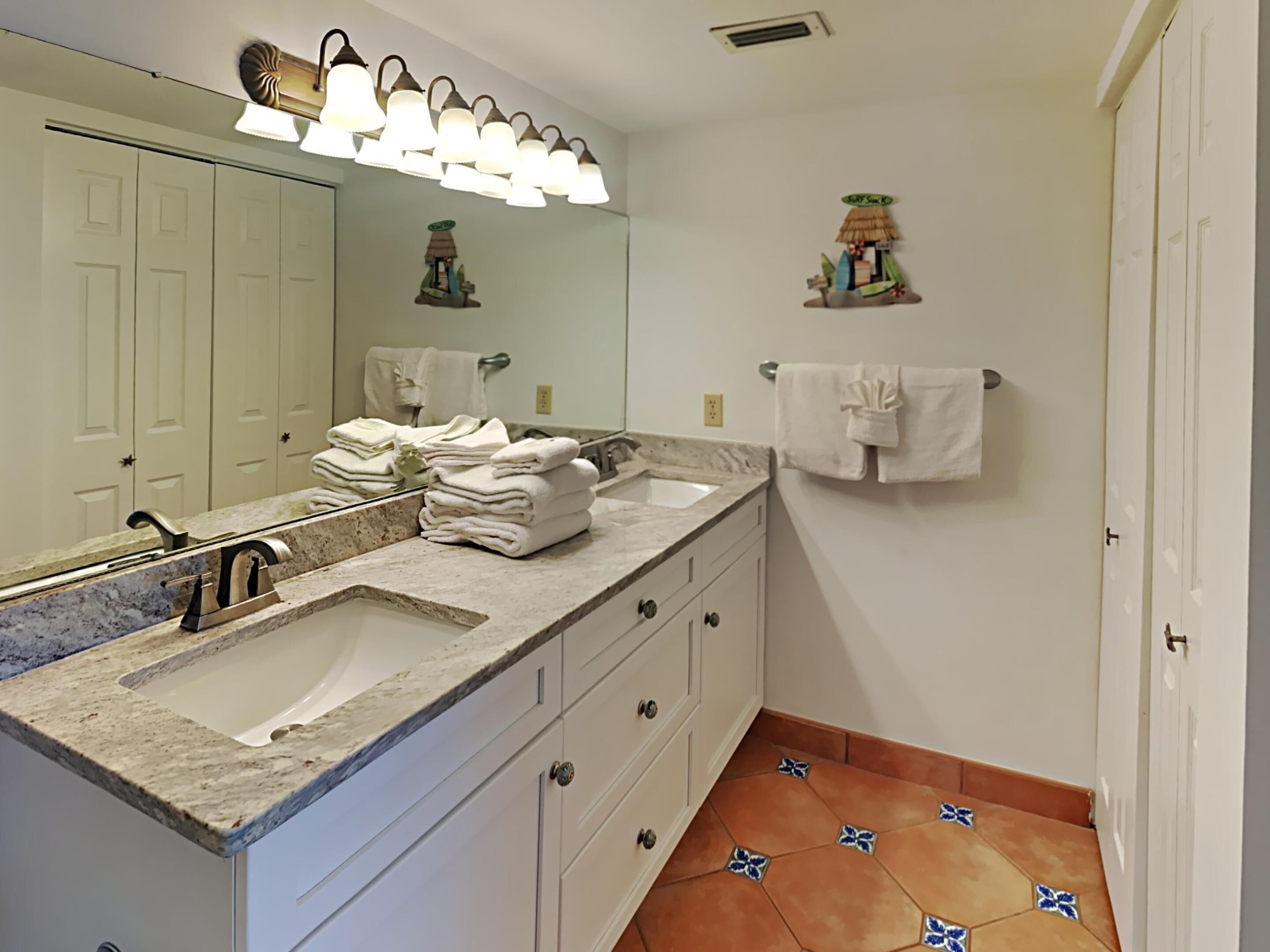 A bathroom with a large mirror, two sinks, a towel rack, and a decorative shelf.