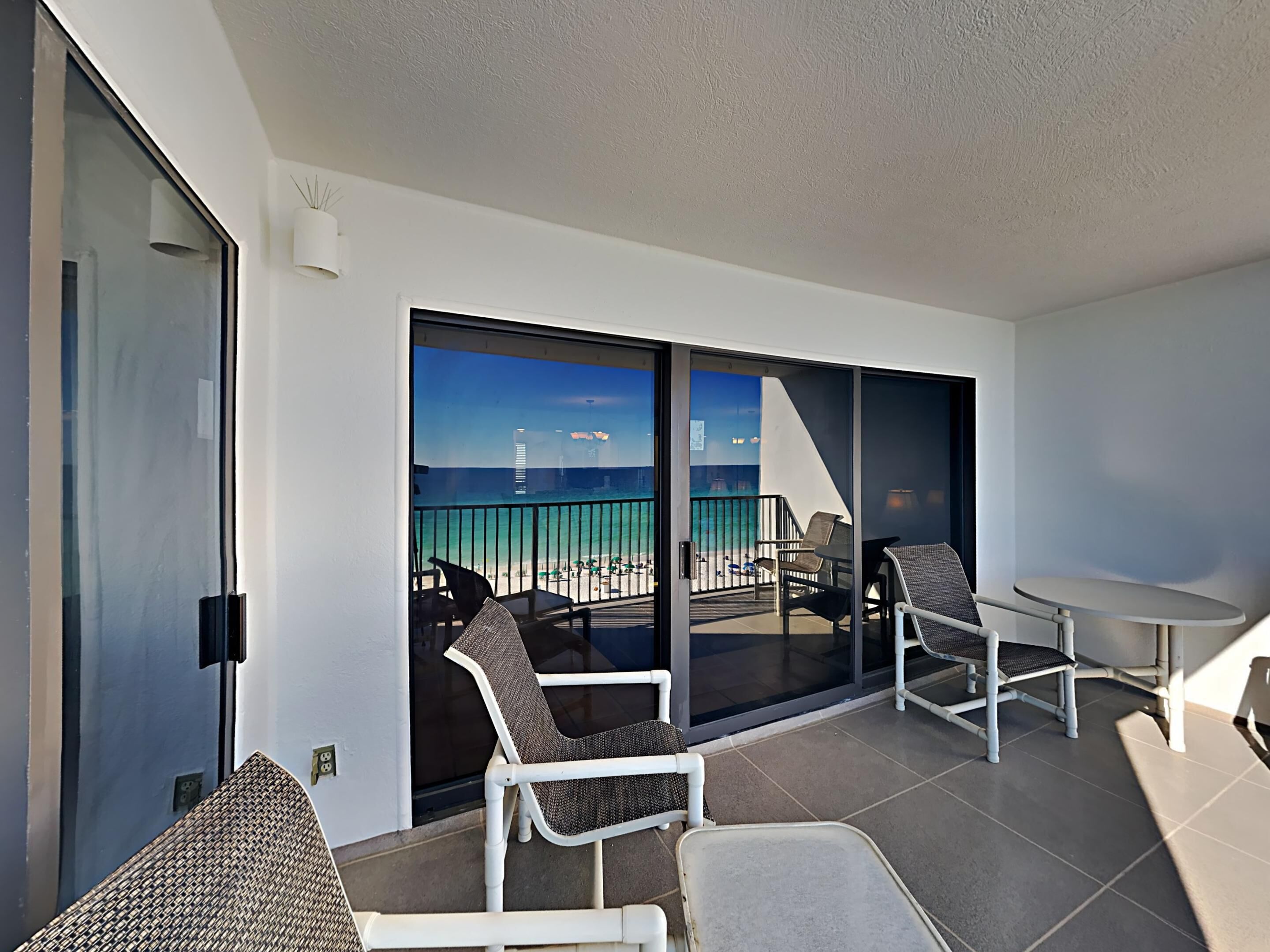 En balkon med udsigt over havet og stranden, møbleret med stole og et bord.