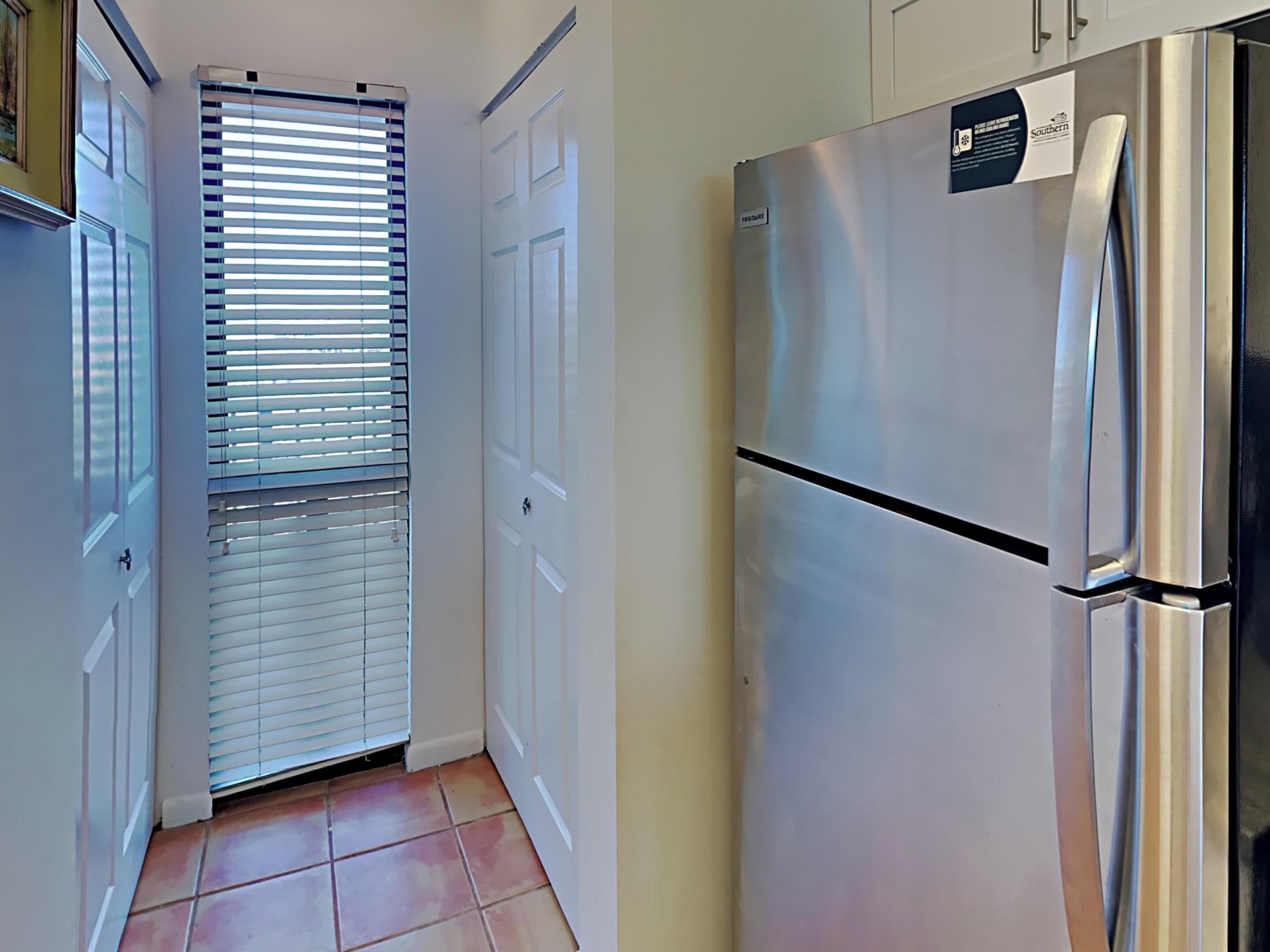 A kitchen with a stainless steel refrigerator, white cabinets, and a window with blinds.