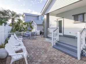 A patio with white chairs and a table, a white fence, and a house with a porch. - Day Dream by Southern Vacation Rentals (Destin)