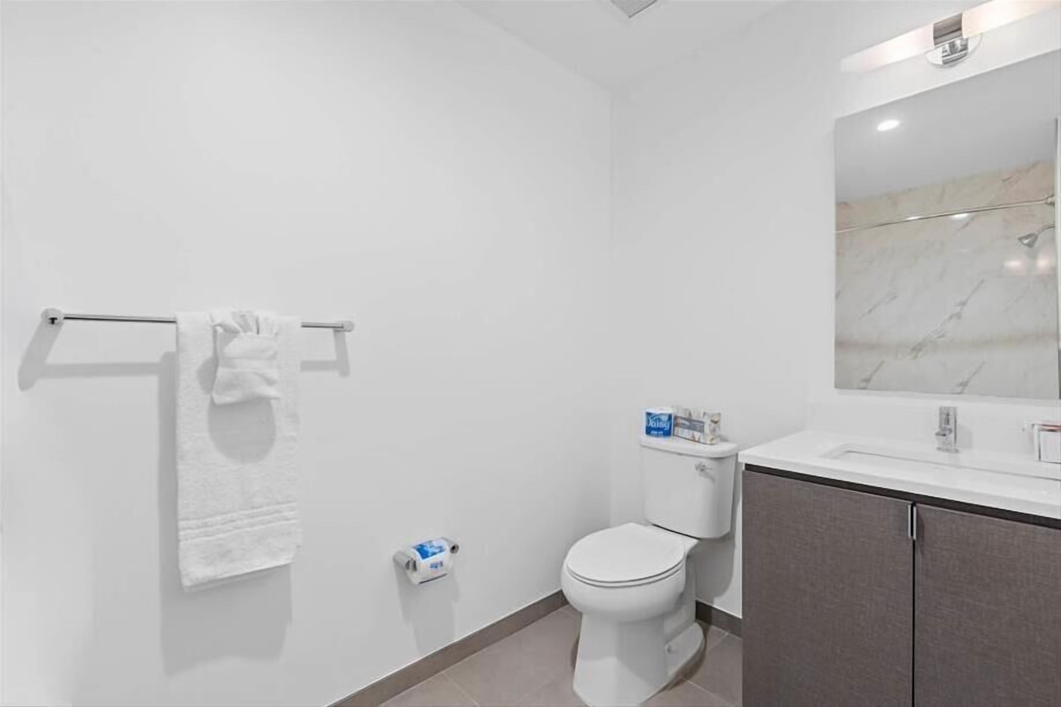 Un baño moderno con inodoro, toallero, lavamanos y espejo.