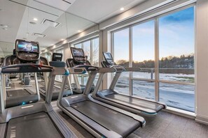 Ein Fitnessraum mit Laufbändern, einem Fernseher und großen Fenstern mit Blick auf eine verschneite Landschaft.
