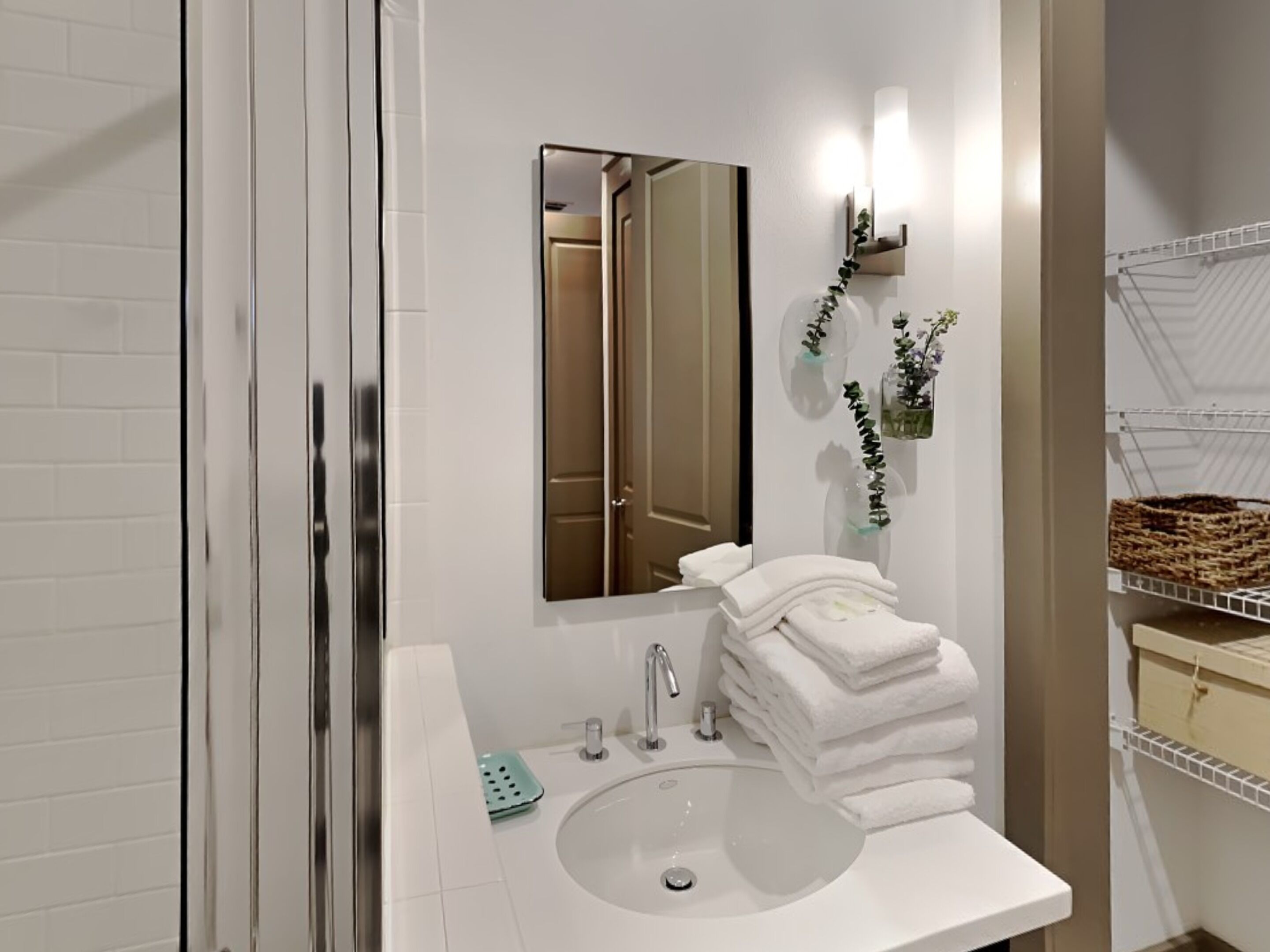 Une salle de bain avec un lavabo blanc, un miroir, un porte-serviettes avec des serviettes pliées et une petite étagère avec un panier.