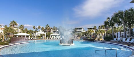 A large circular pool with a central fountain, surrounded by palm trees and lounge chairs.