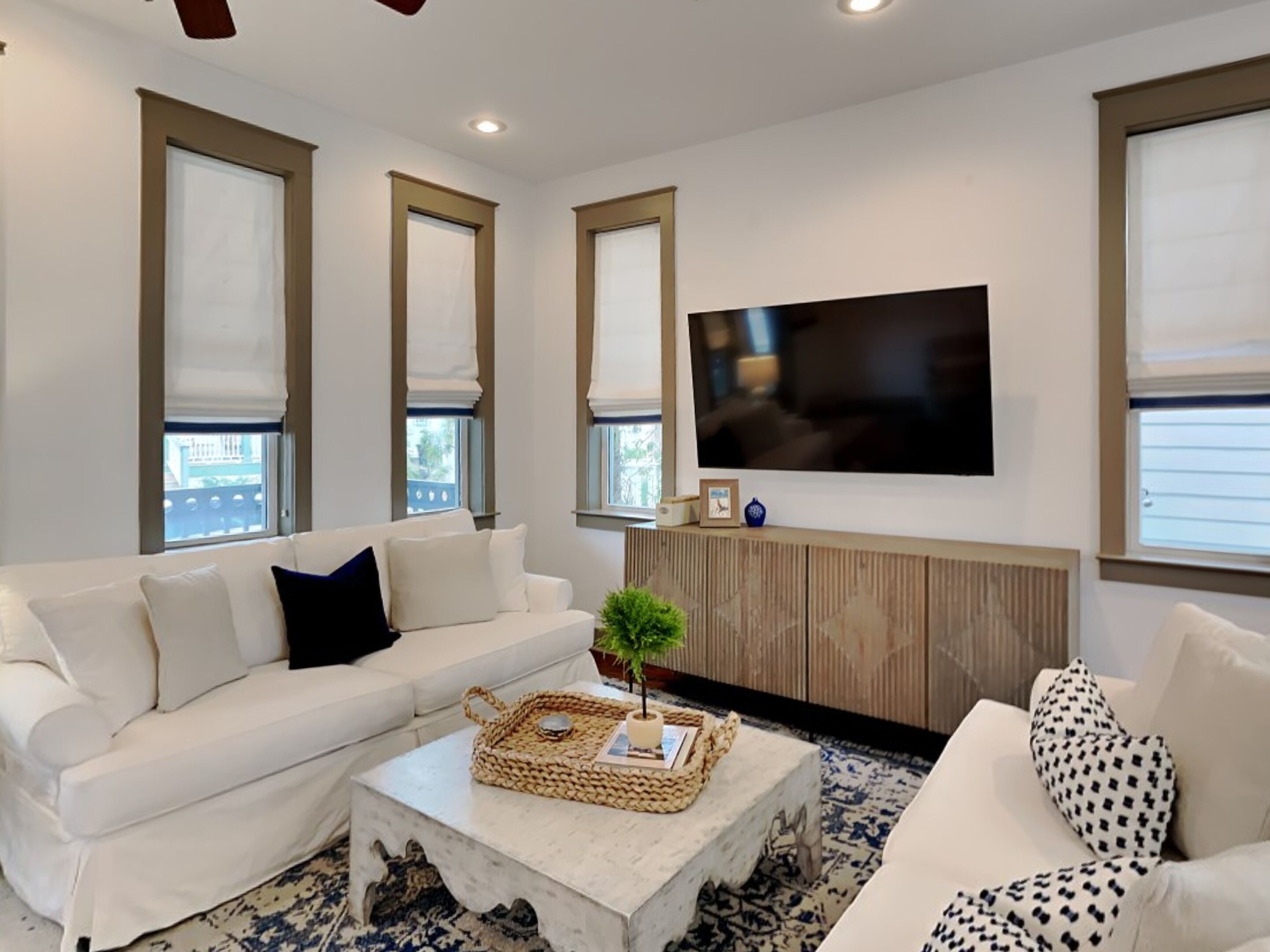 A living room with a white sofa, a coffee table, and a TV mounted on the wall.