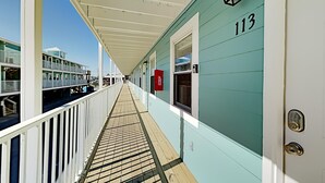 Un corridoio con un pavimento in legno, una ringhiera bianca e un edificio color acquamarina con il numero 113.
