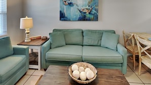 Un soggiorno con un divano color acquamarina, un tavolino con una lampada, un cesto pieno di oggetti rotondi e un quadro appeso al muro.