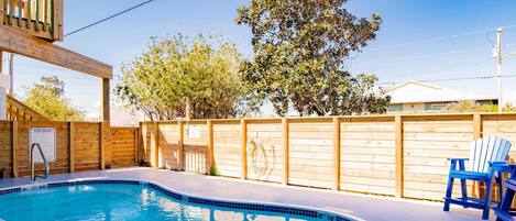 A swimming pool with a wooden deck, a wooden fence, and a blue chair.