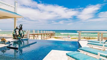 A pool area with a view of the ocean, a wooden deck, and lounge chairs.