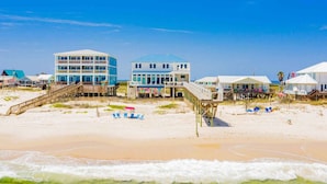 A beachfront property with multiple buildings, including a two-story house with a balcony and a larger building with a blue roof. - Mural Manor on Ponce by Southern Vacation Rentals (Gulf Shores)
