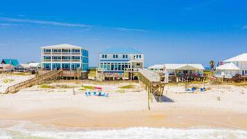 A beachfront property with multiple buildings, including a two-story house with a balcony and a larger building with a blue roof.
