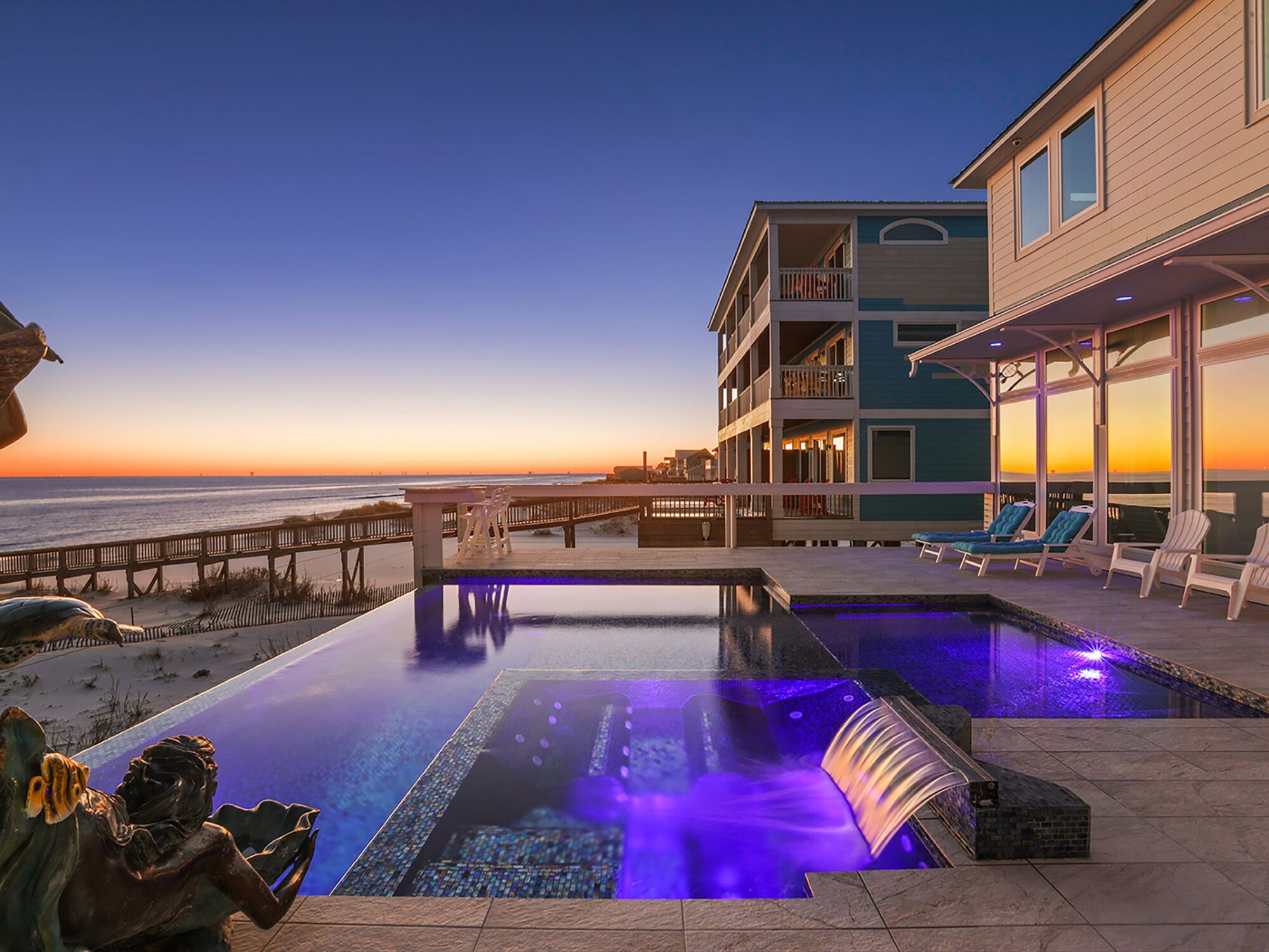 A pool area with a sunset view, lounge chairs, and a building with balconies.