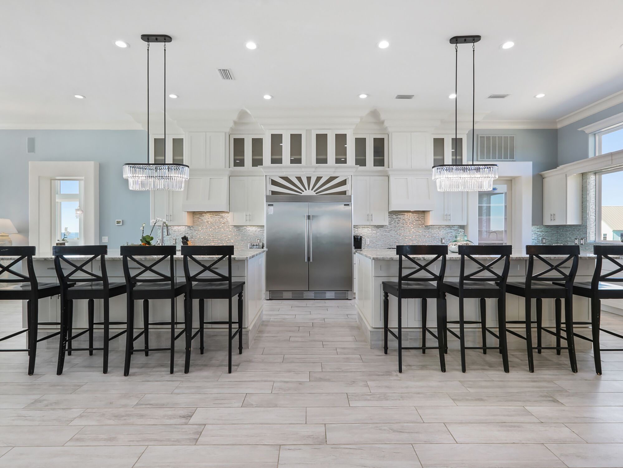 A modern kitchen with white cabinetry, a stainless steel refrigerator, and black chairs.
