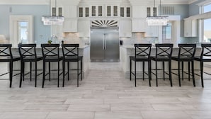 A modern kitchen with white cabinetry, a stainless steel refrigerator, and black chairs. - Mural Manor on Ponce by Southern Vacation Rentals (Gulf Shores)