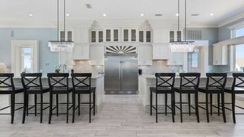 A modern kitchen with white cabinetry, a stainless steel refrigerator, and black chairs.
