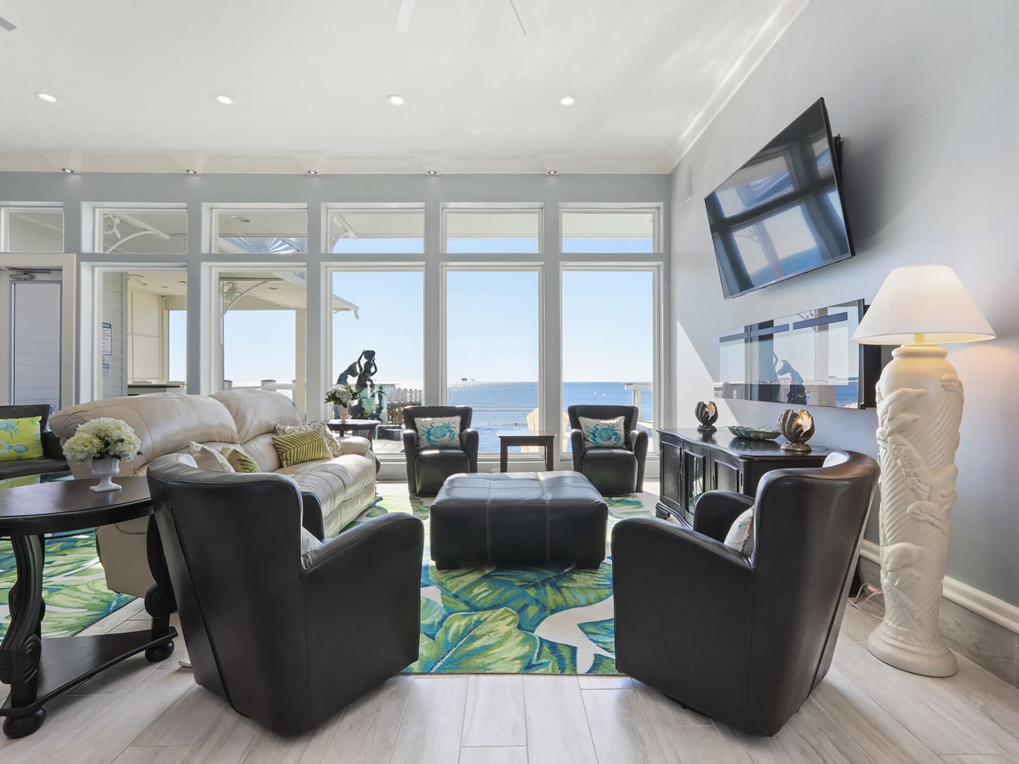A spacious living room with a view of the ocean, featuring a sofa, armchairs, a coffee table, and a TV mounted on the wall.
