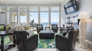 A spacious living room with a view of the ocean, featuring a sofa, armchairs, a coffee table, and a TV mounted on the wall. - Mural Manor on Ponce by Southern Vacation Rentals (Gulf Shores)