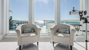 A room with two armchairs, a telescope, and a view of the ocean through large windows. - Mural Manor on Ponce by Southern Vacation Rentals (Gulf Shores)