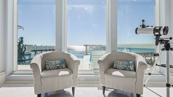 A room with two armchairs, a telescope, and a view of the ocean through large windows.