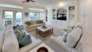 A spacious living room with a large sofa, a coffee table, and a television mounted on the wall. There are multiple windows providing a view of the outdoors. - Margarita by Southern Vacation Rentals (Destin)