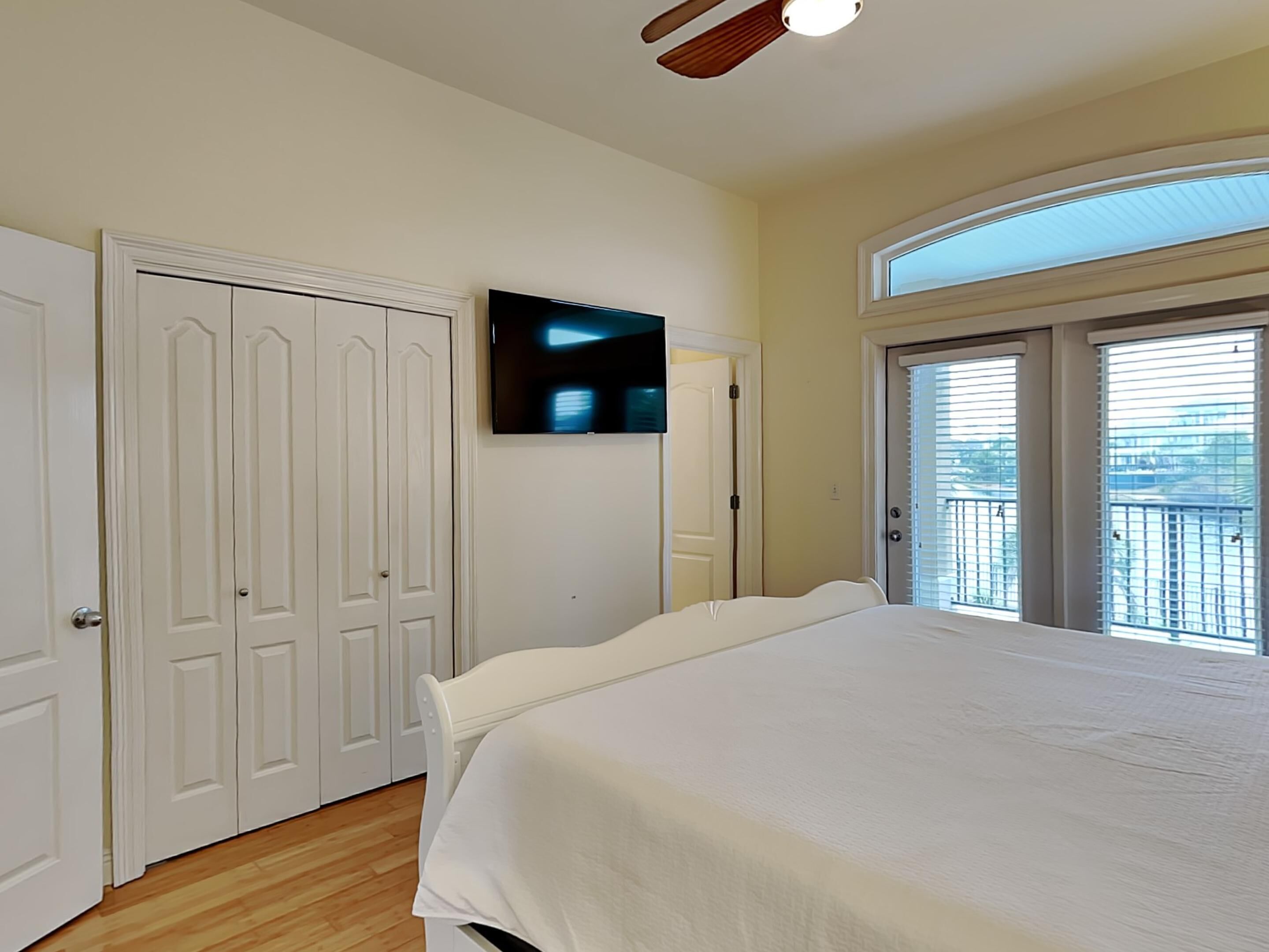 A bedroom with a bed, a television on the wall, a door, and a balcony with a view.