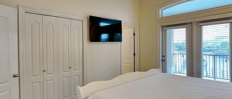 A bedroom with a bed, a television on the wall, a door, and a balcony with a view.