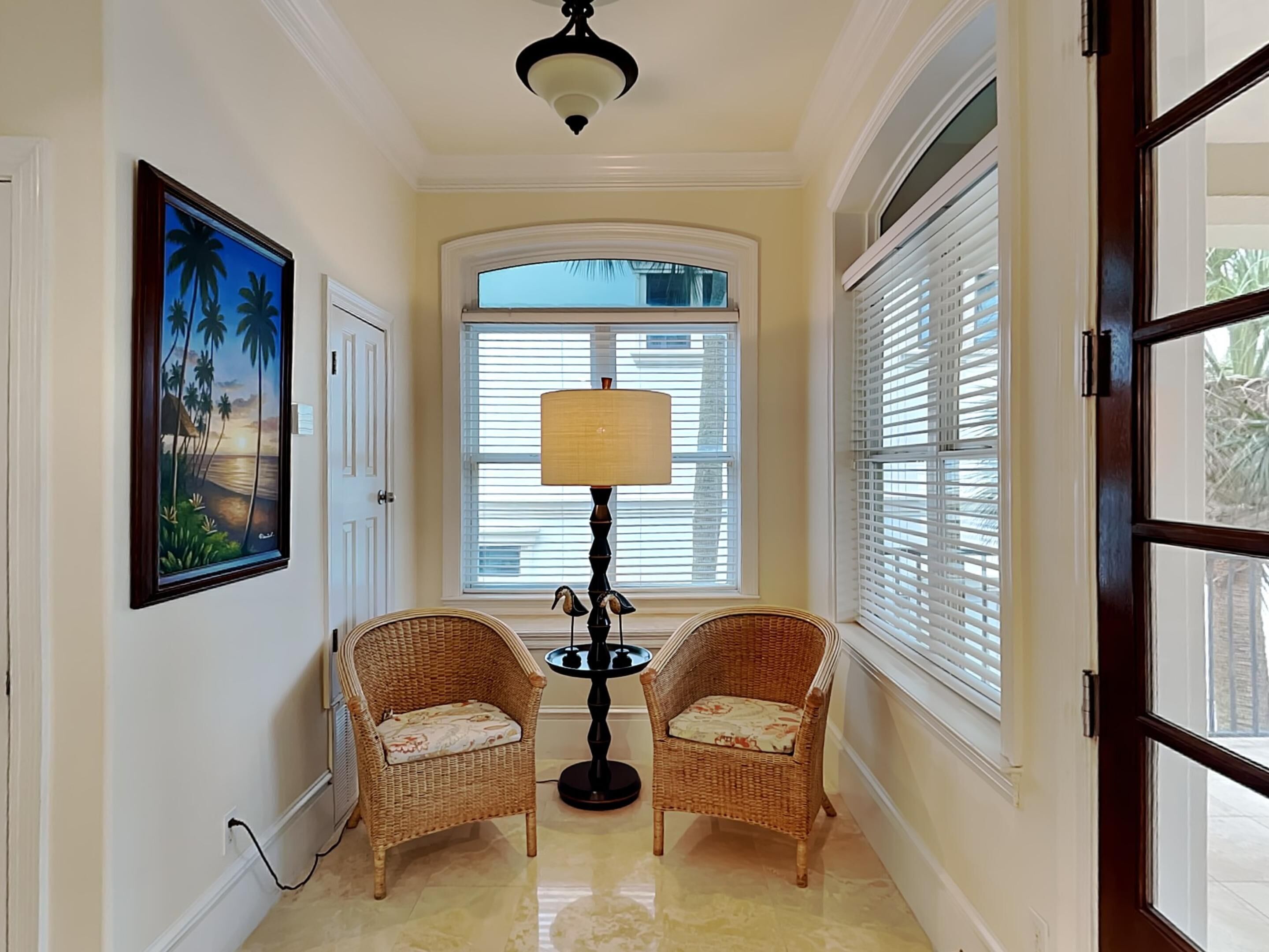 A hallway with two wicker chairs, a floor lamp, and a painting of a beach scene.