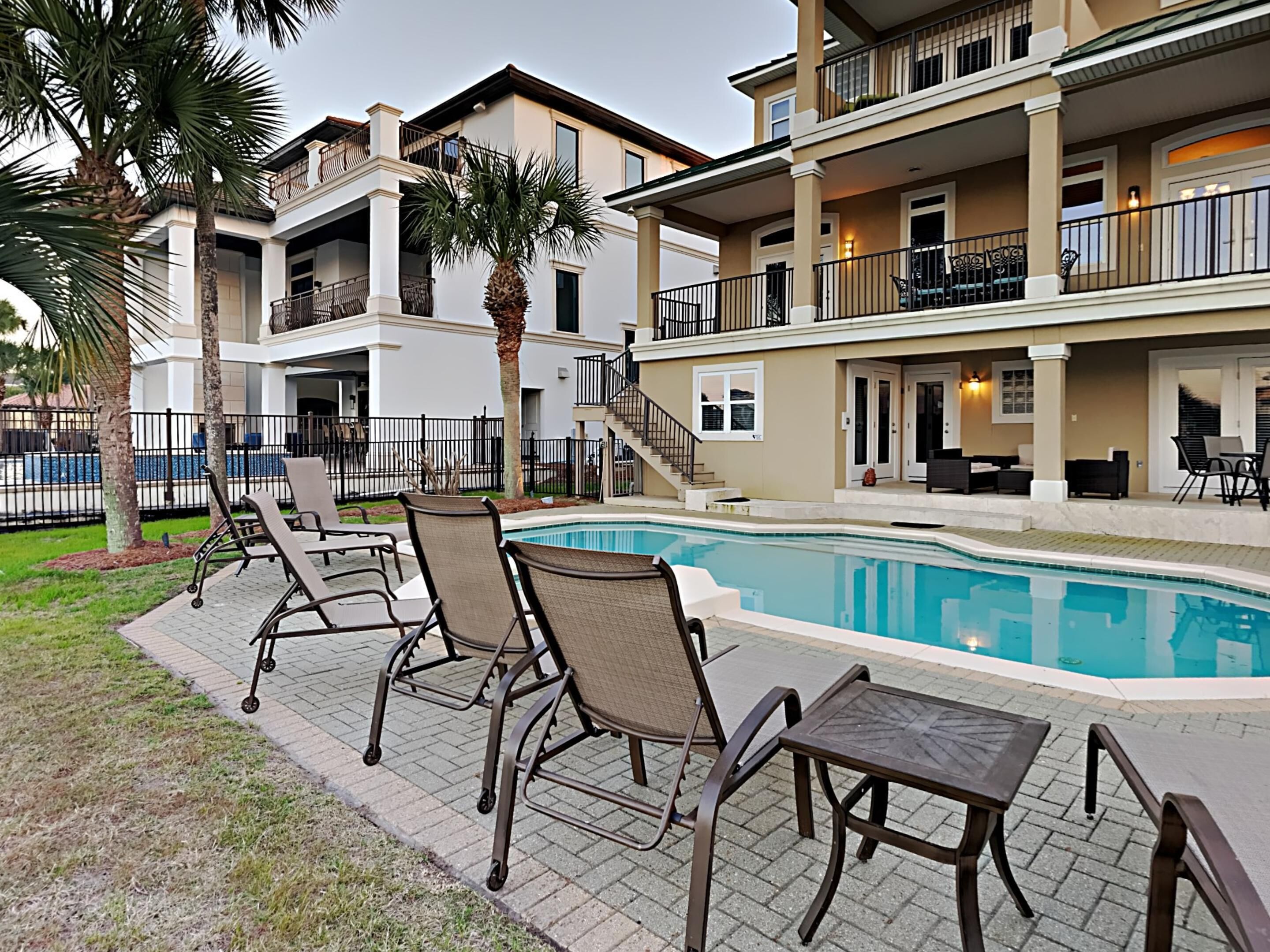 A two-story building with a swimming pool, outdoor seating, and palm trees.