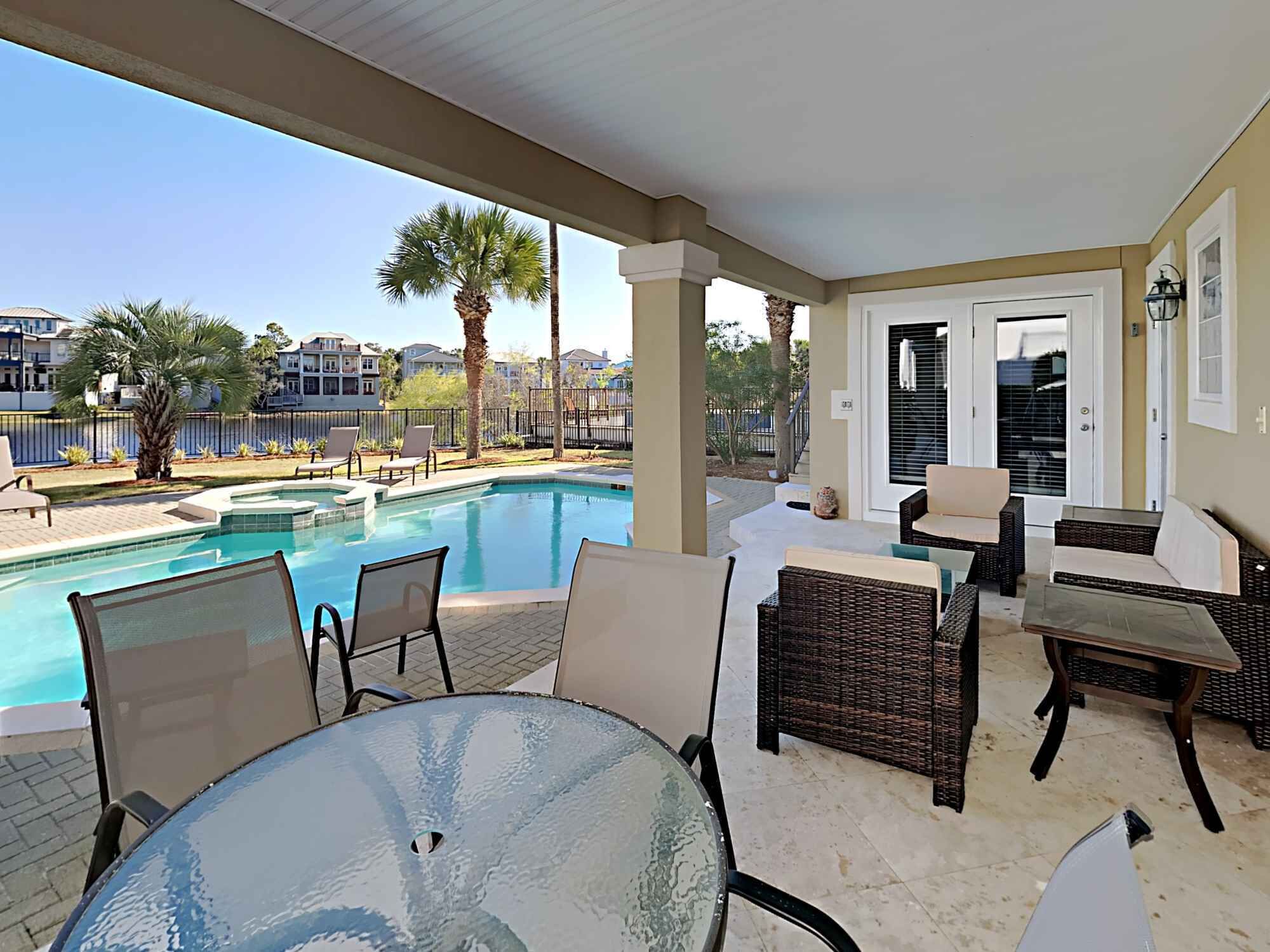 Ein überdachter Außenbereich mit Pool, Korbmöbeln und Blick auf die Nachbarhäuser.