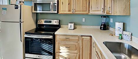 A kitchen with wooden cabinets, a stainless steel refrigerator, a microwave, an oven, a toaster, a blender, and a sink.