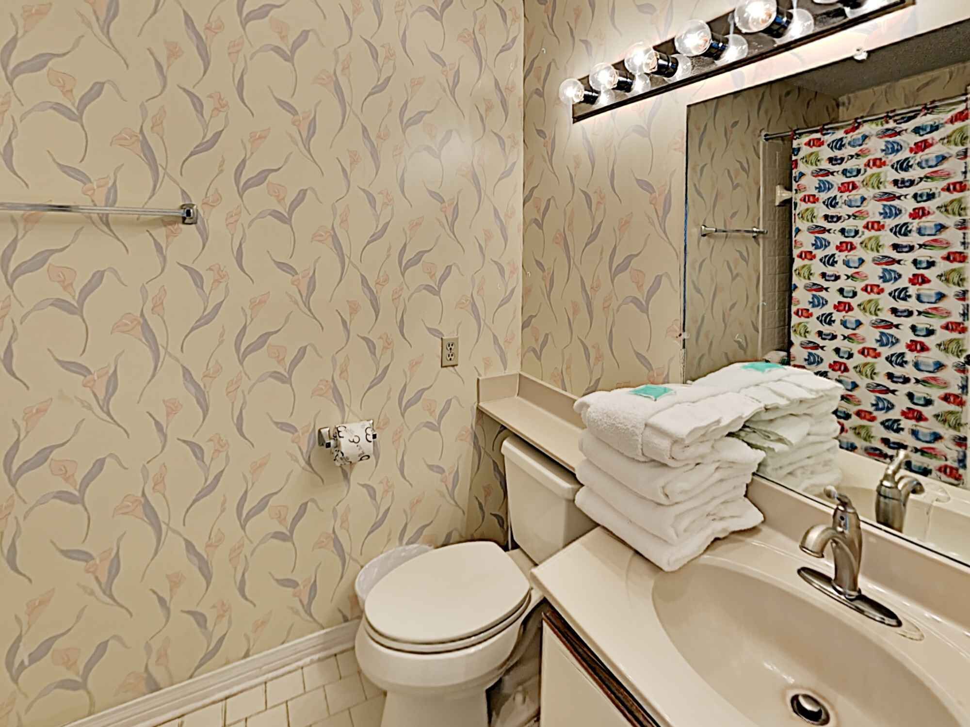 Een badkamer met bloemenbehang, een toilet, een wastafel met spiegel en een handdoekrek.