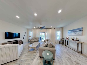 Relax in this stylish living room with a large flat-screen TV, comfortable sofa, and a view of the outdoors through large windows.