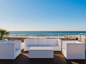 Enjoy the ocean view from this seaside terrace with a sofa and two ottomans.