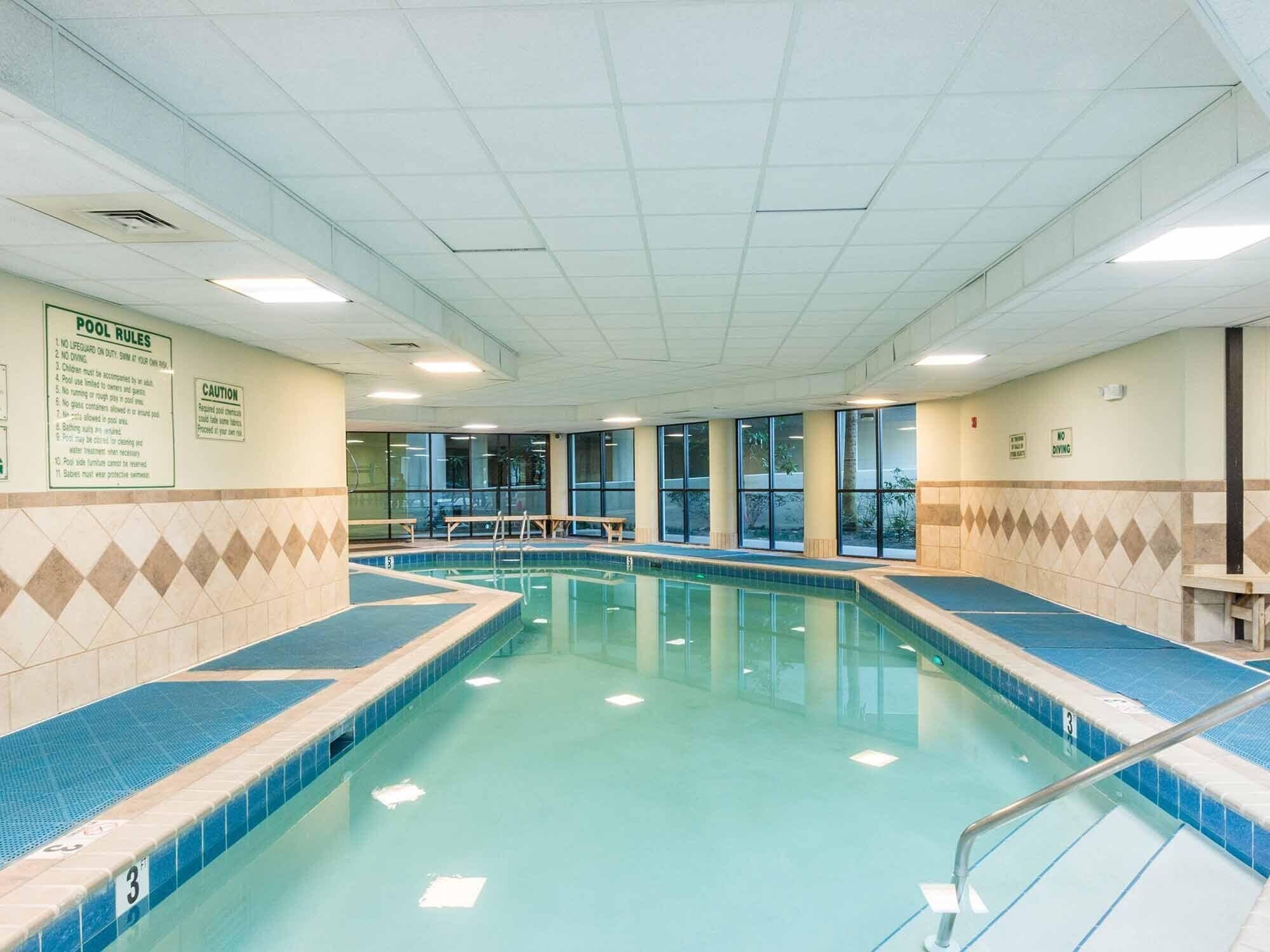 Une grande piscine intérieure, avec des règles d’utilisation clairement affichées sur le mur, des bancs le long des bords et un sol carrelé.