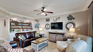 A living room with a brown leather sofa, a beige sofa, a coffee table, a TV, and a ceiling fan. - Phoenix on the Bay by Southern Vacation Rentals (Orange Beach)