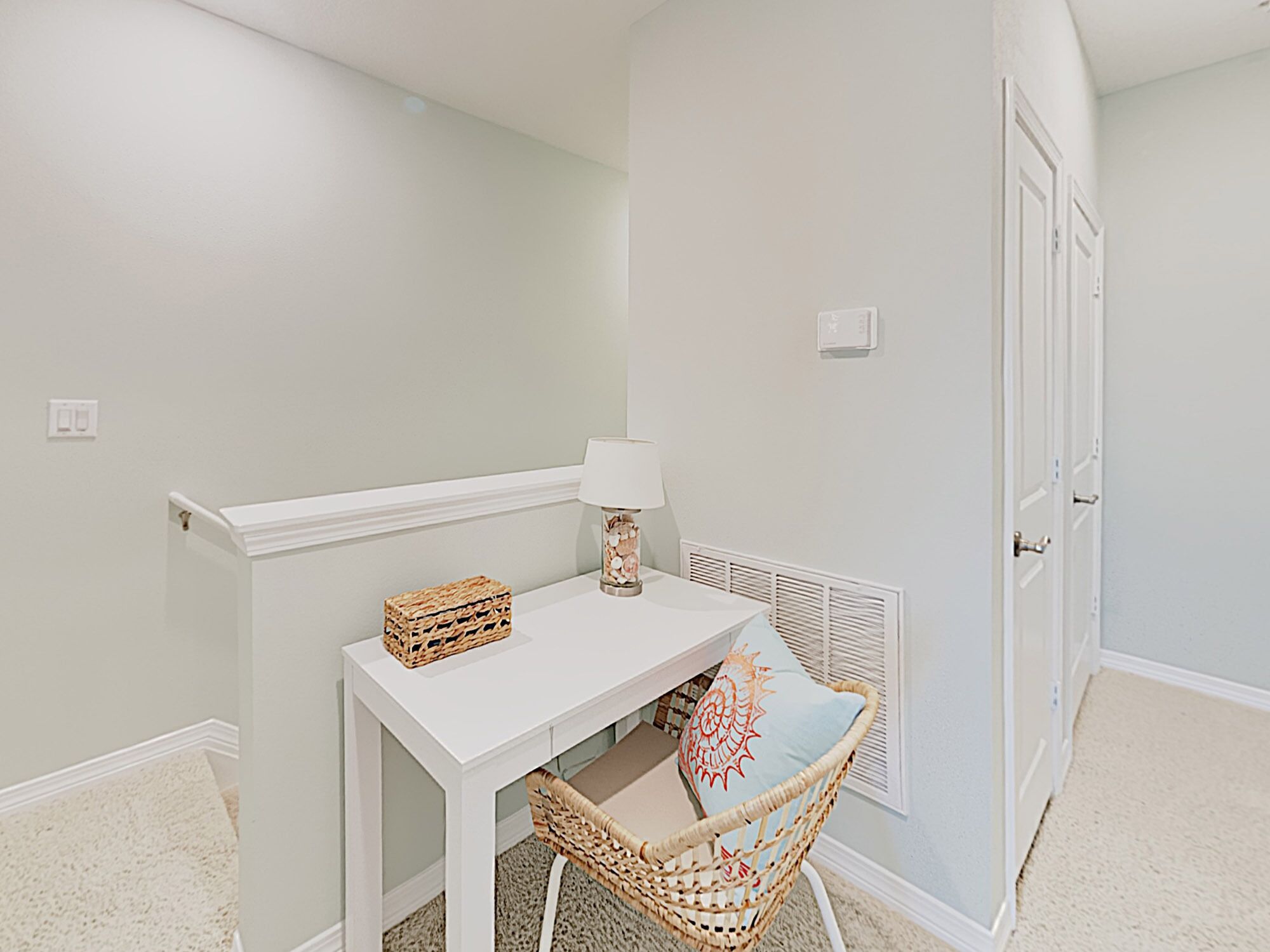A small, neatly arranged room with a white table, wicker chair, and a lamp.