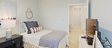 A bedroom with a bed, bedside table, lamp, and a television on a dresser.