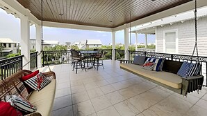 A covered patio with a wooden ceiling, a dining table with chairs, a sofa with cushions, and a swing. - Seabreeze Cabana by Southern Vacation Rentals (Panama City Beach)