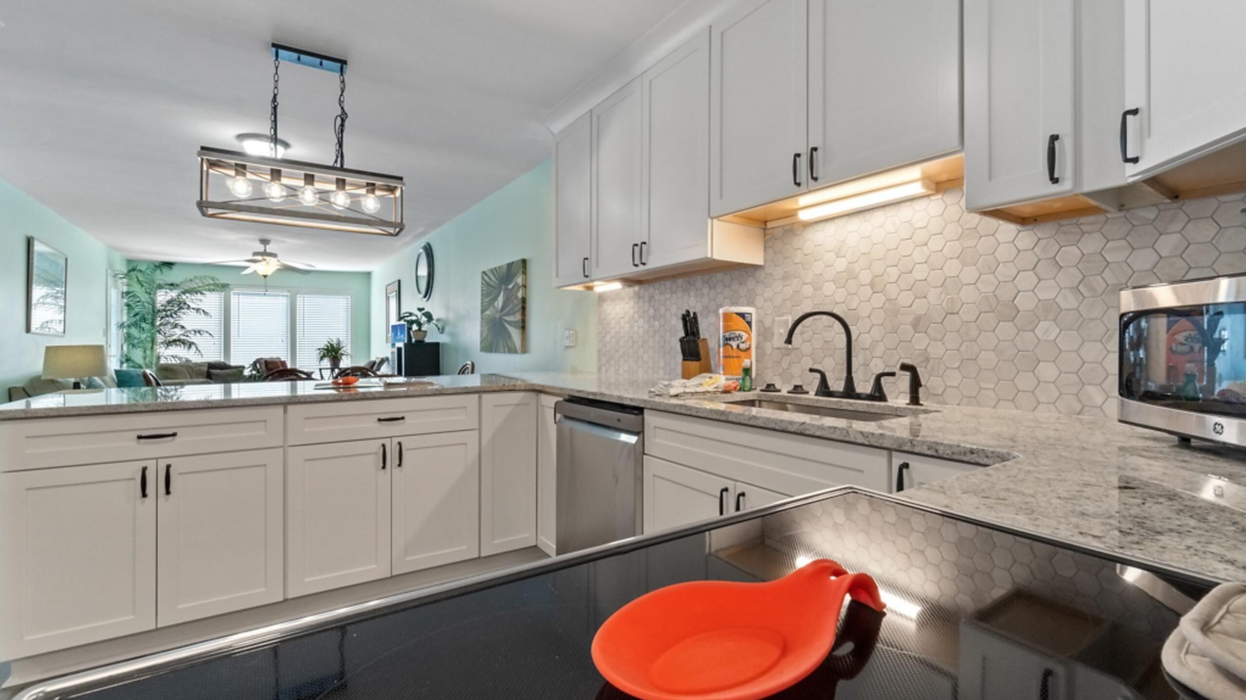 A modern kitchen with white cabinets, a black countertop, and a glass dining table.