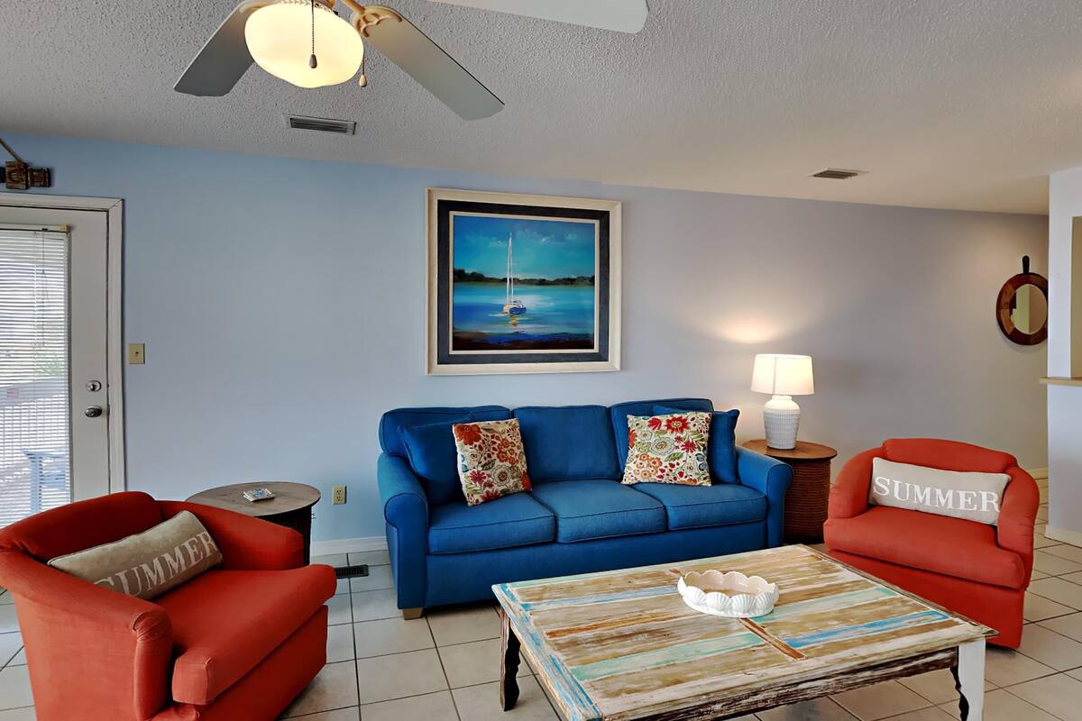 A living room with a blue sofa, red armchairs, a coffee table, and a painting of a sailboat.