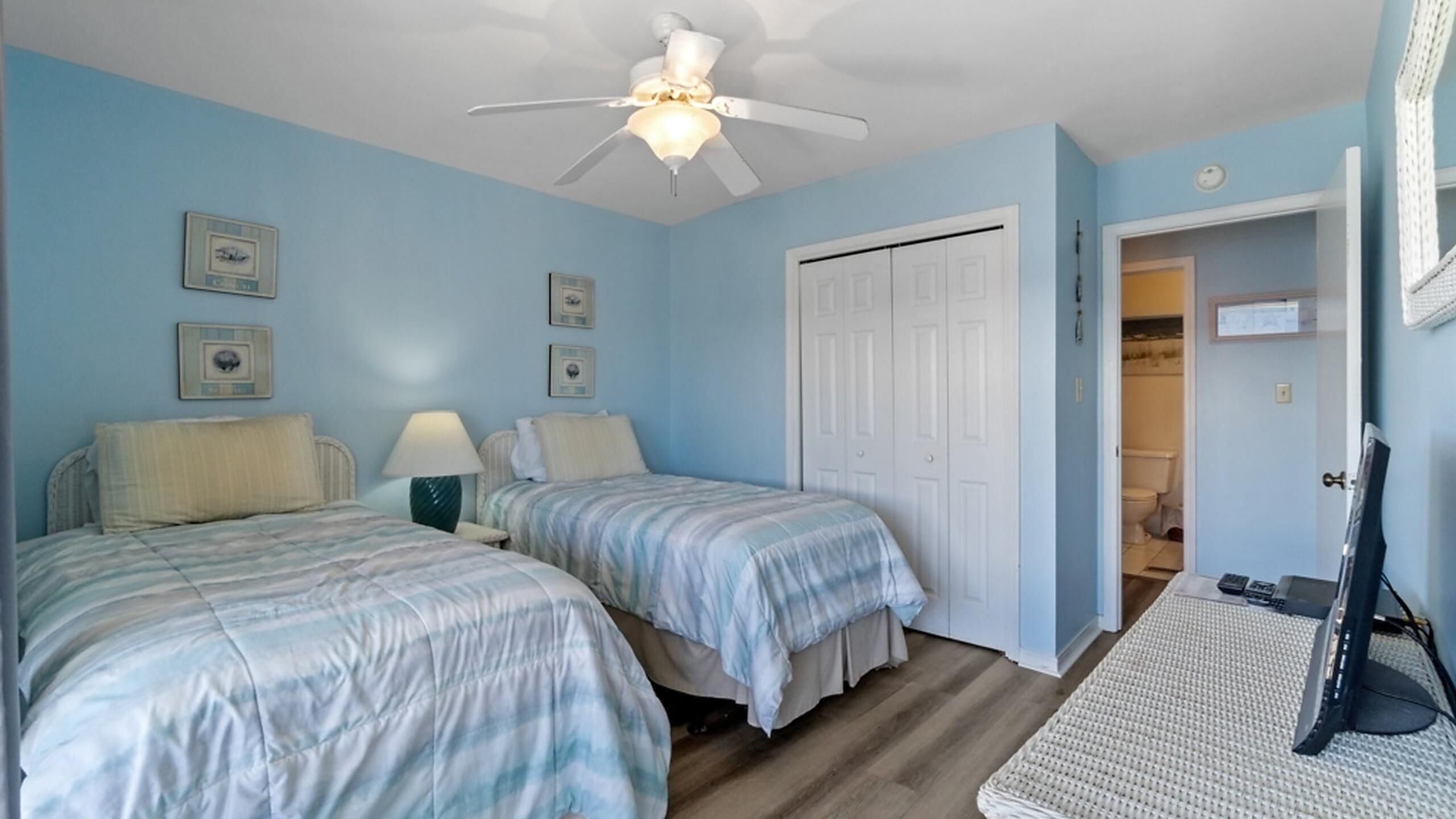A bedroom with two beds, a ceiling fan, and a door leading to a bathroom.