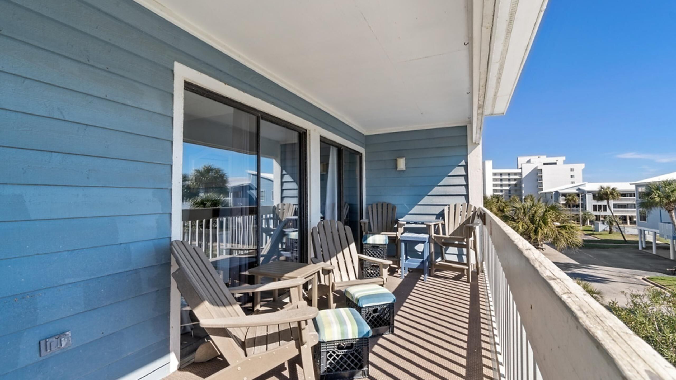 A balcony with outdoor seating, including chairs and a table, overlooking a residential area with palm trees and buildings.