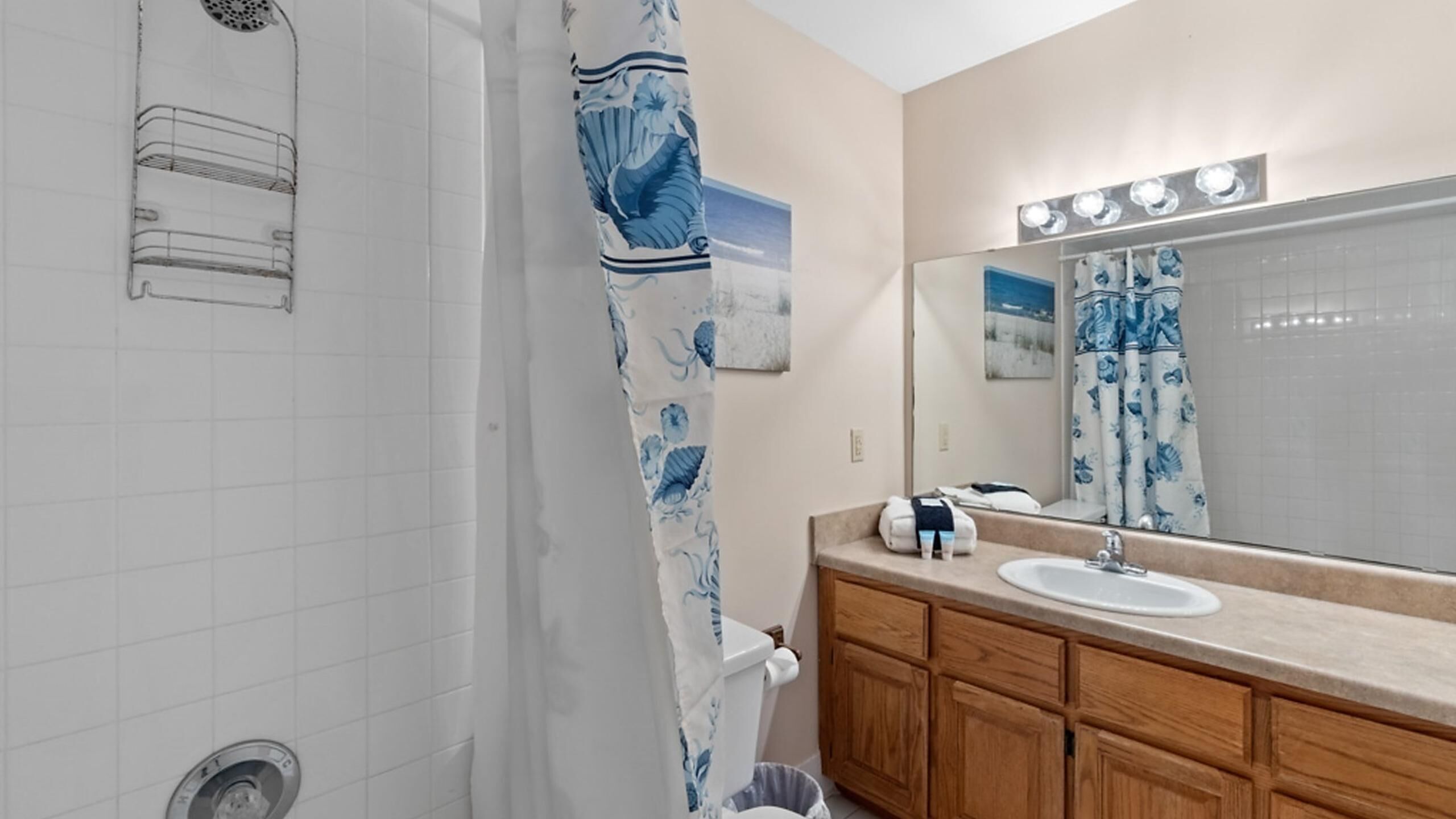 A bathroom with a shower, a sink, a mirror with lights, and a towel rack.