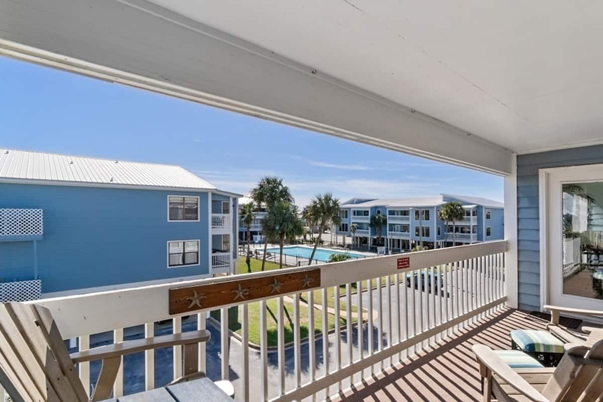 A balcony with wooden chairs and a view of a swimming pool and other buildings.