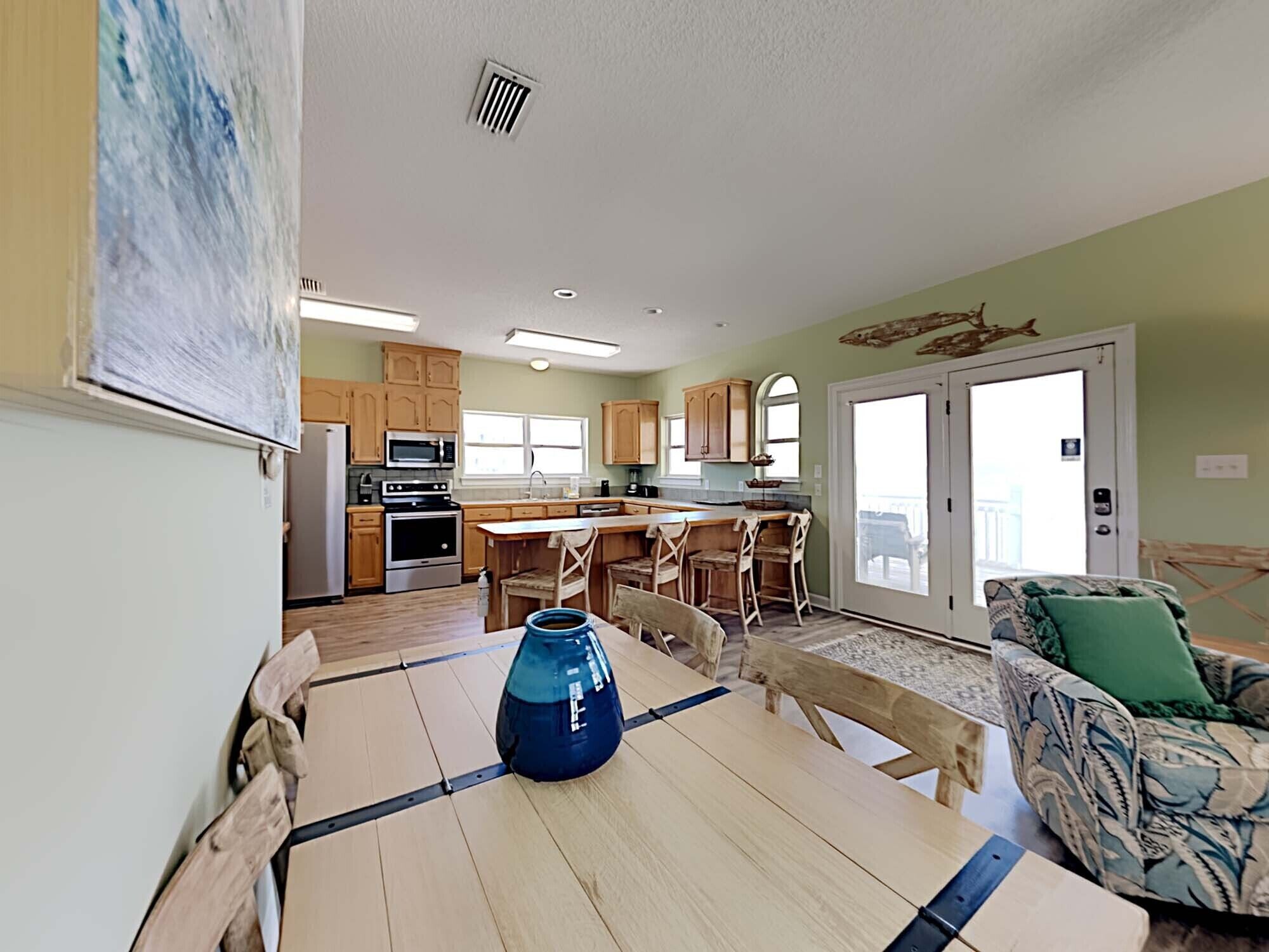 A spacious kitchen with wooden cabinets, a central island with bar stools, and a dining table with a blue vase.