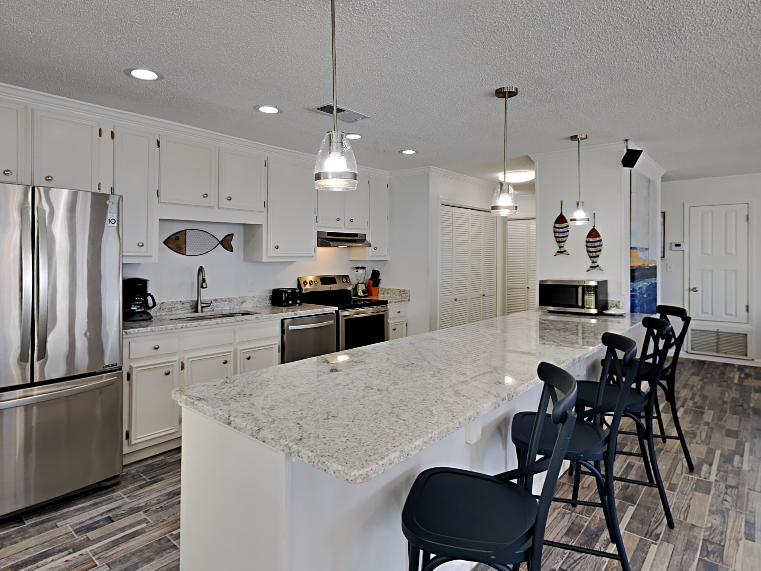 A modern kitchen with white cabinets, stainless steel appliances, and a granite island with bar stools.