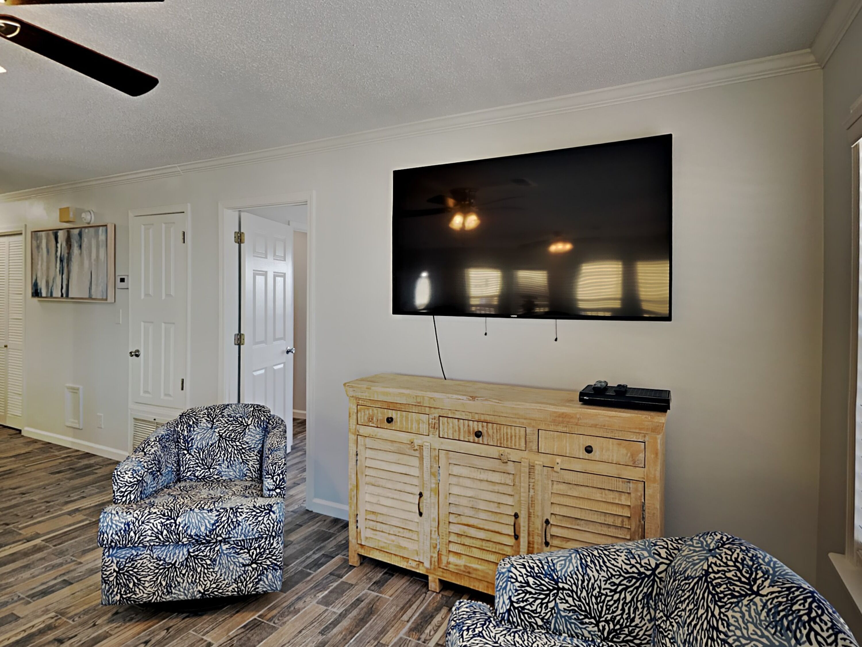 Una sala de estar con sofás estampados, un mueble de madera y un televisor de pantalla plana grande montado en la pared.