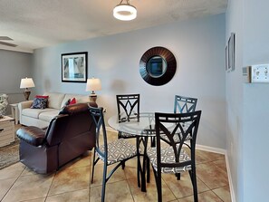 A living room with a brown leather sofa, a glass coffee table, and patterned chairs. There is a framed picture on the wall and a round mirror above the table. - Phoenix III by Southern Vacation Rentals (Orange Beach)